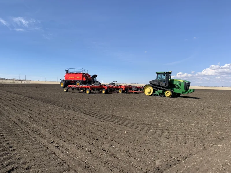 Green tractor pulling red seeding equipment across a freshly worked field